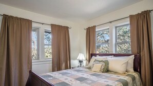 A bedroom with a wooden bed, a quilt, and curtains.