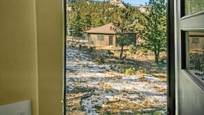 A view from inside a room looking out to a house surrounded by trees and a rocky landscape.