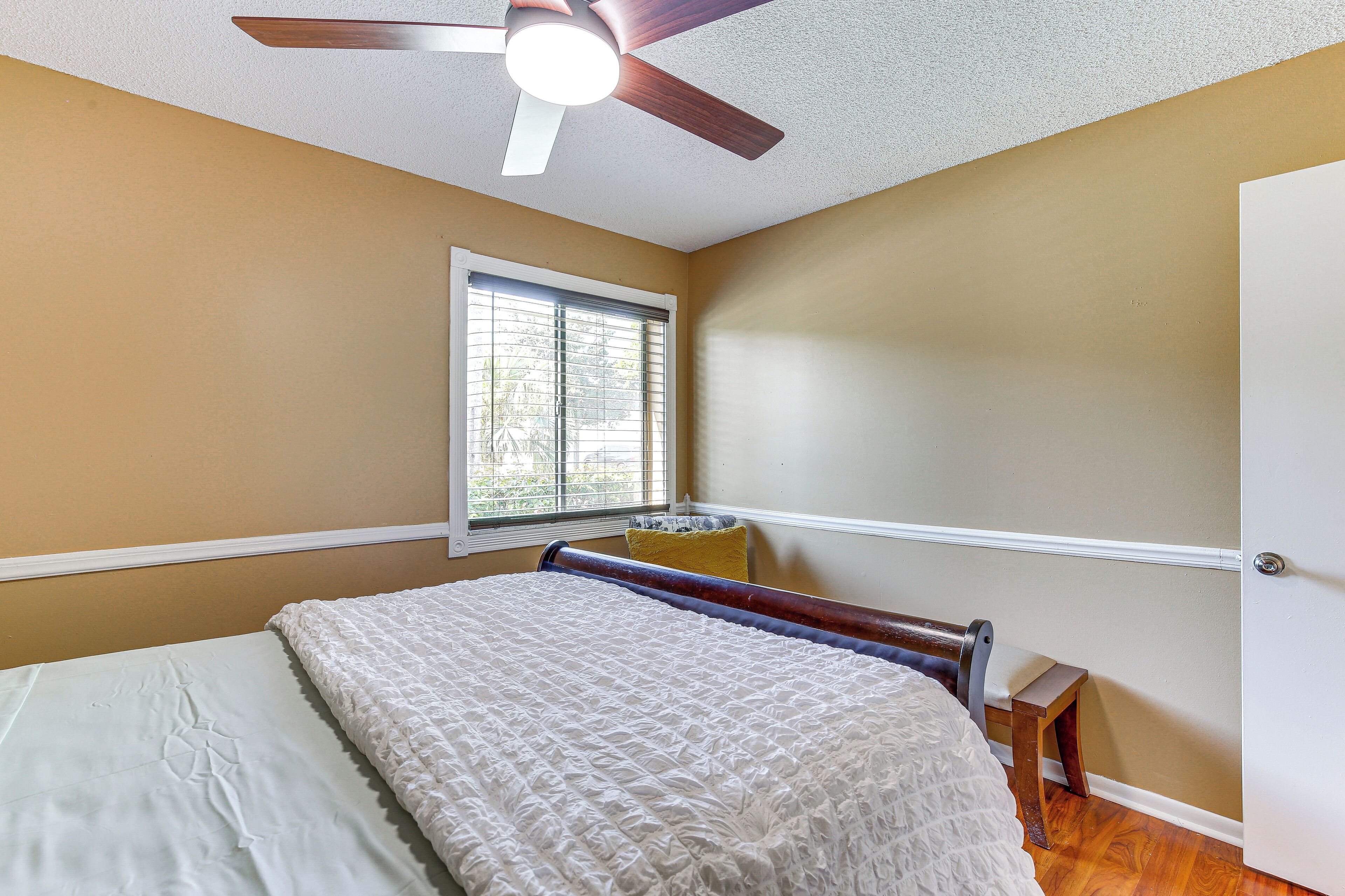 Une chambre à coucher avec un lit, un ventilateur de plafond, une fenêtre avec des stores et une porte.