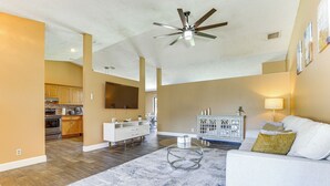 Un salon spacieux avec un canapé blanc, une table basse en verre et un ventilateur de plafond.