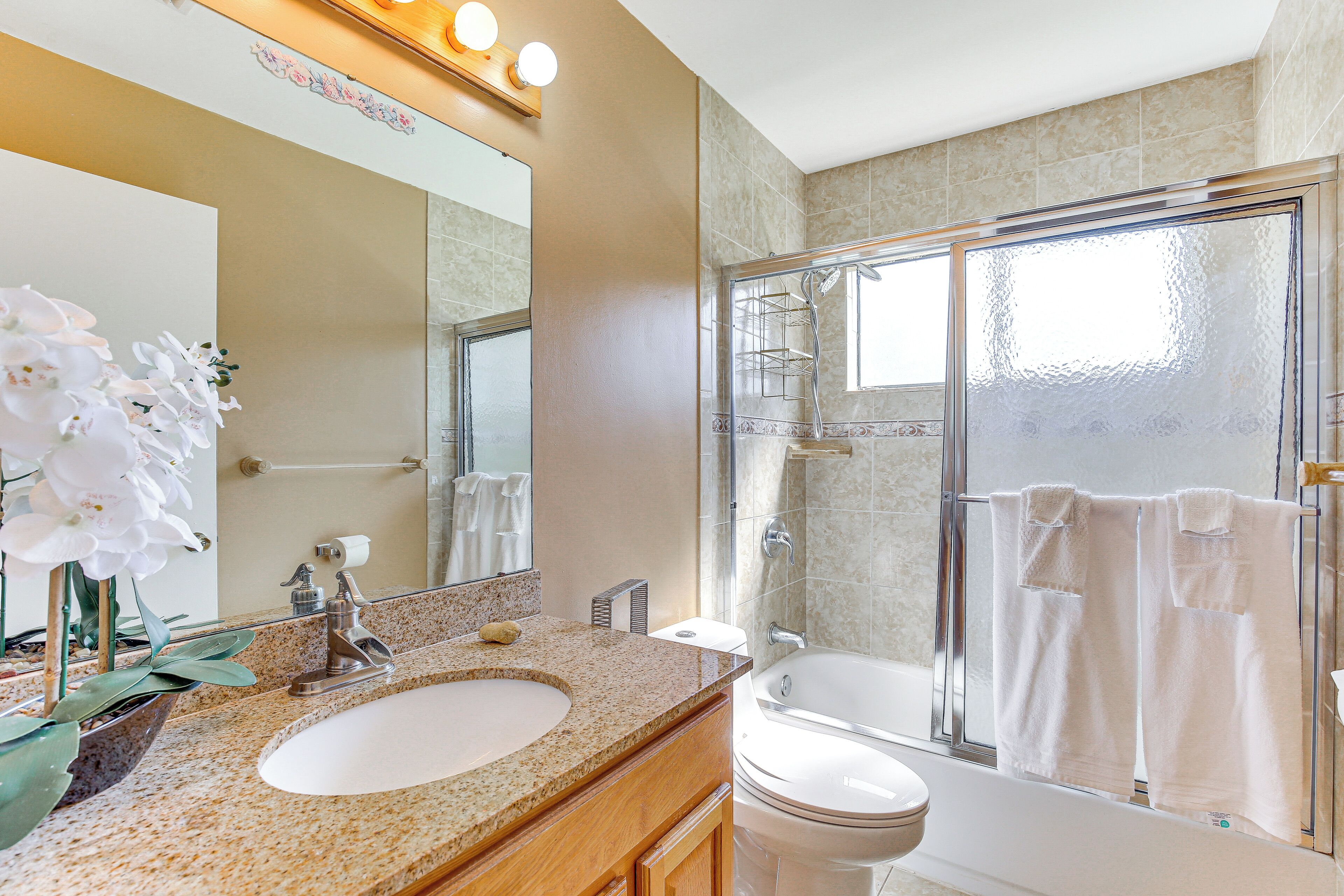 A modern bathroom with a granite countertop sink, a large mirror, a glass-enclosed shower, and a white toilet.