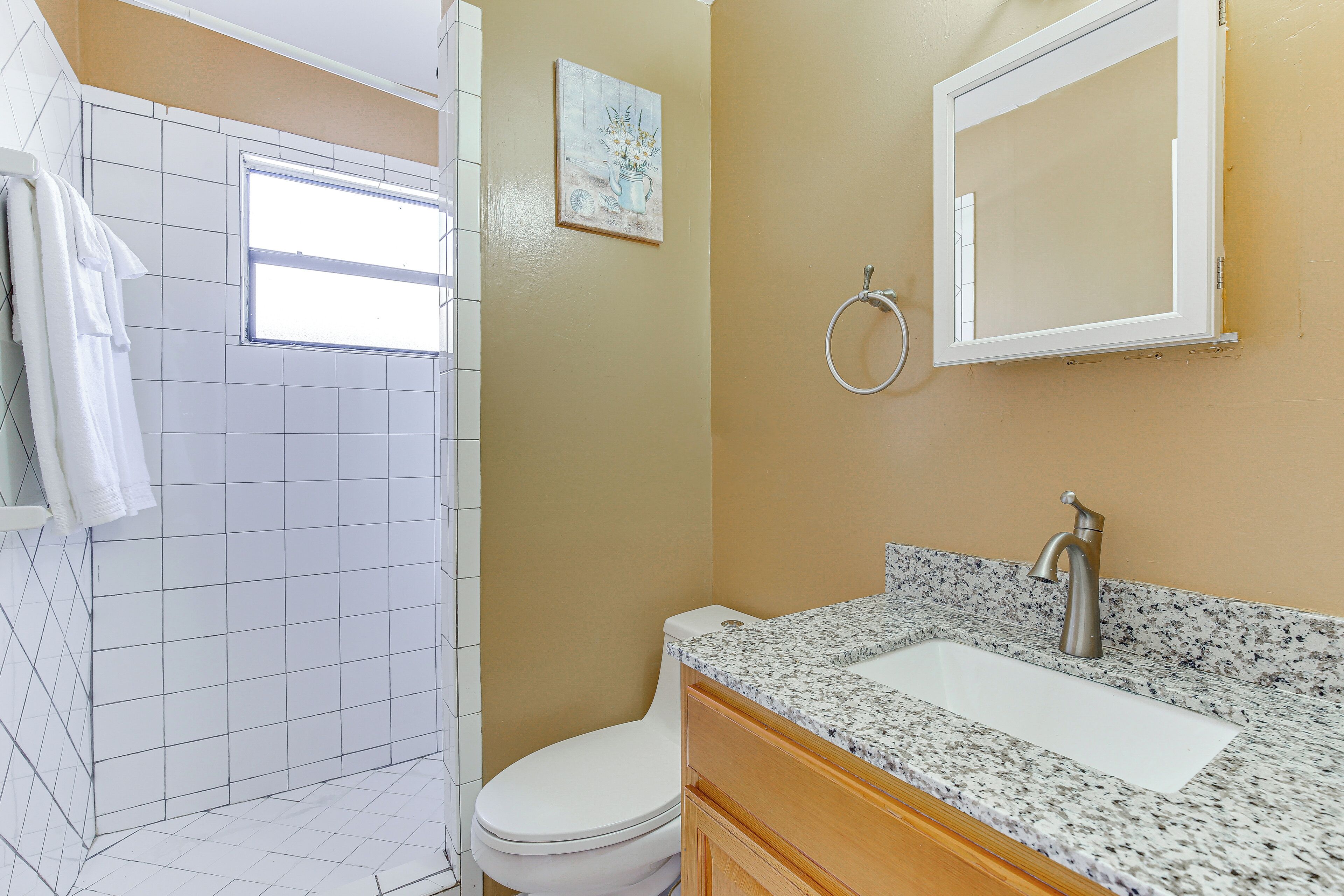 A bathroom with a white toilet, a sink with a granite countertop, and a shower area with white tiles.