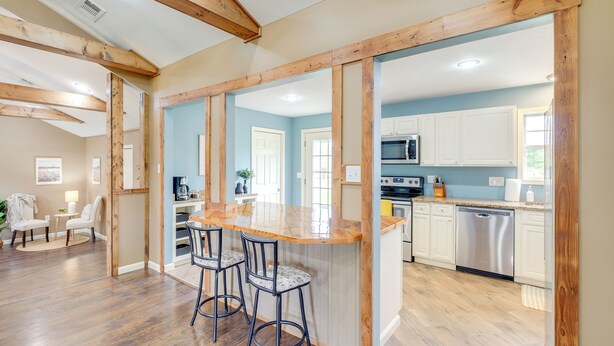 A kitchen with wooden beams, a bar area with stools, and white cabinets.