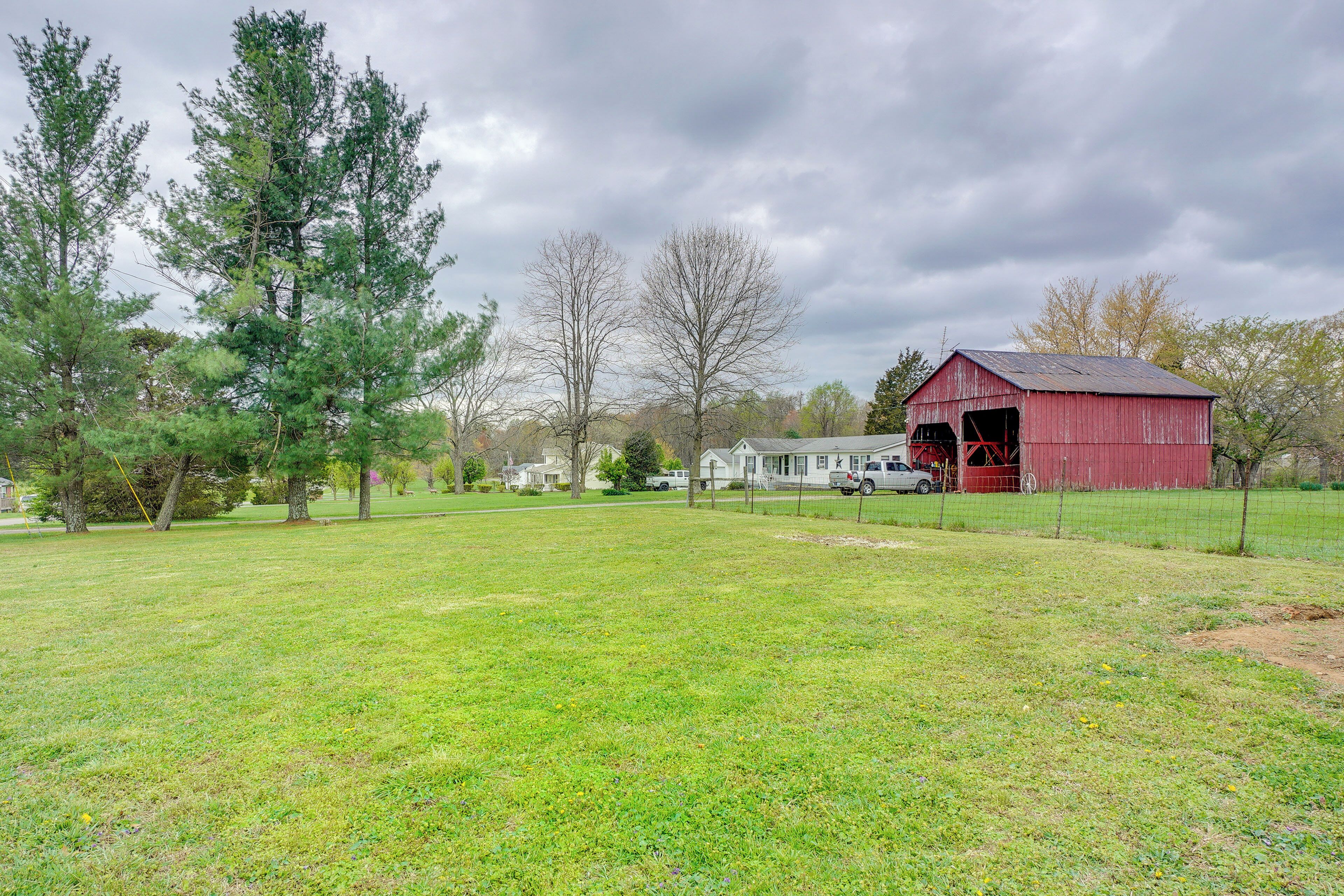 A red barn with a large open door, surrounded by a fenced field and trees.