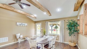 A dining area with a wooden table and chairs, a ceiling fan, and a large window with curtains.