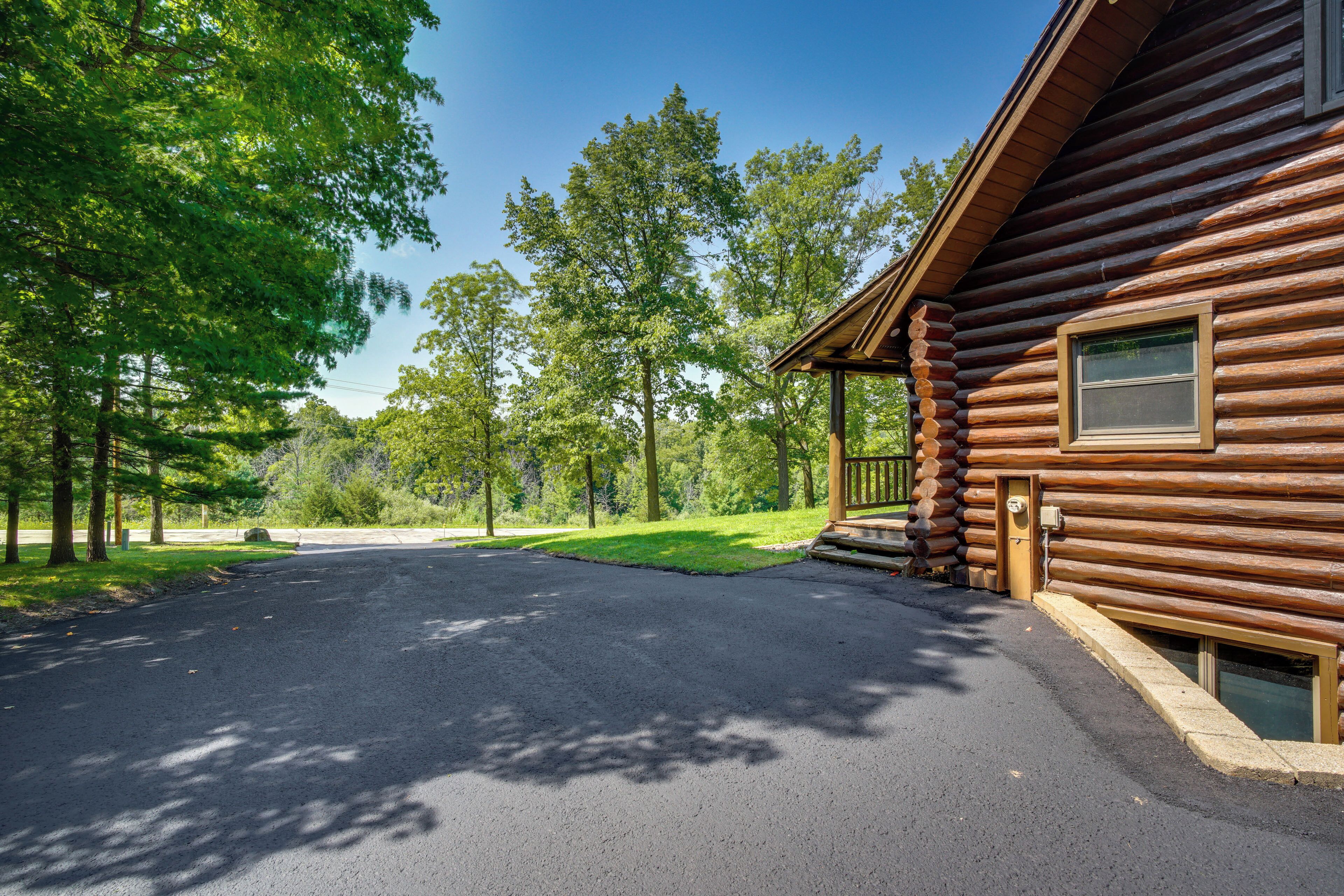 A log cabin with a paved driveway leading to the entrance, surrounded by trees.