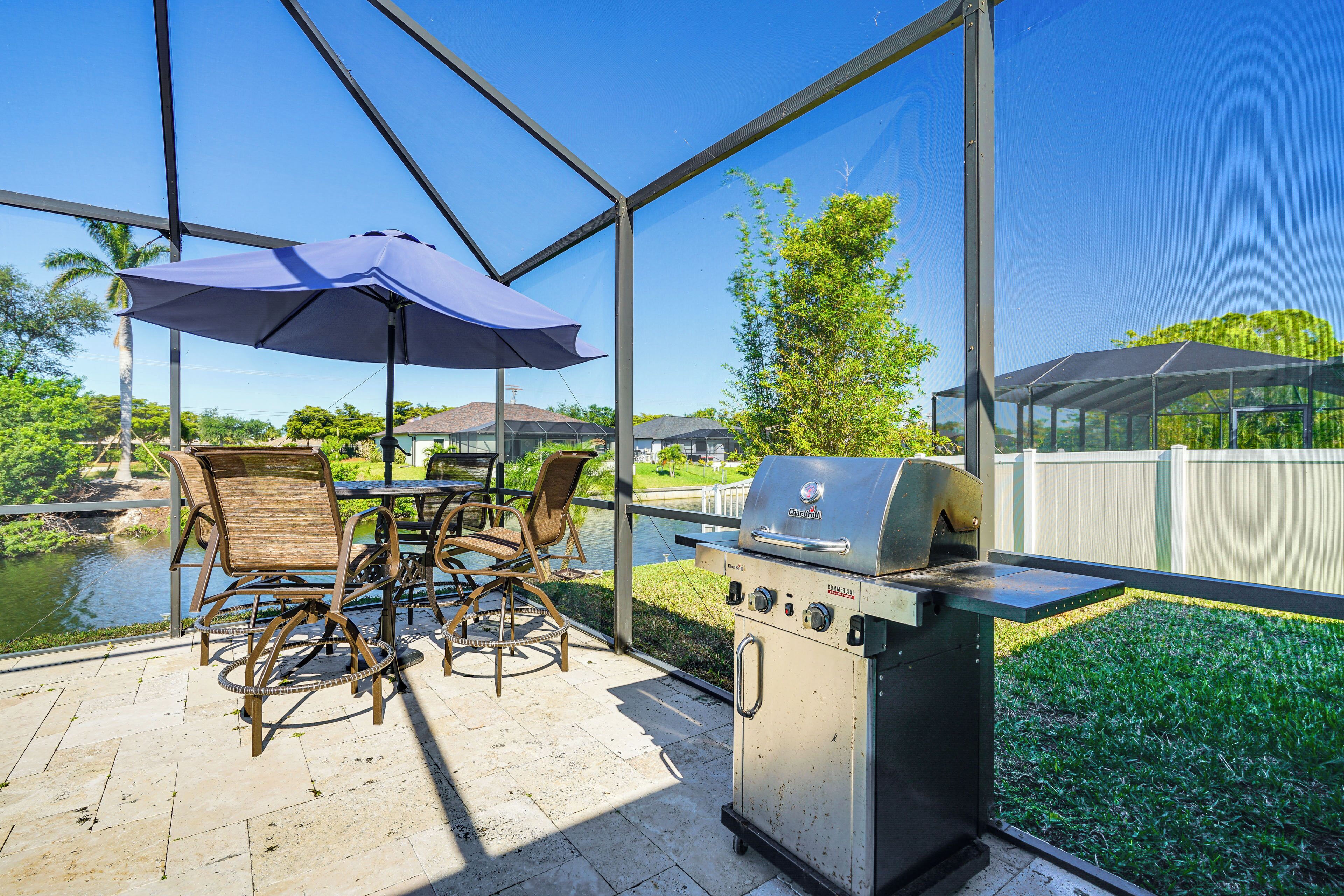 Un patio al aire libre con una parrilla, sillas y sombrillas, con vista a un cuerpo de agua.