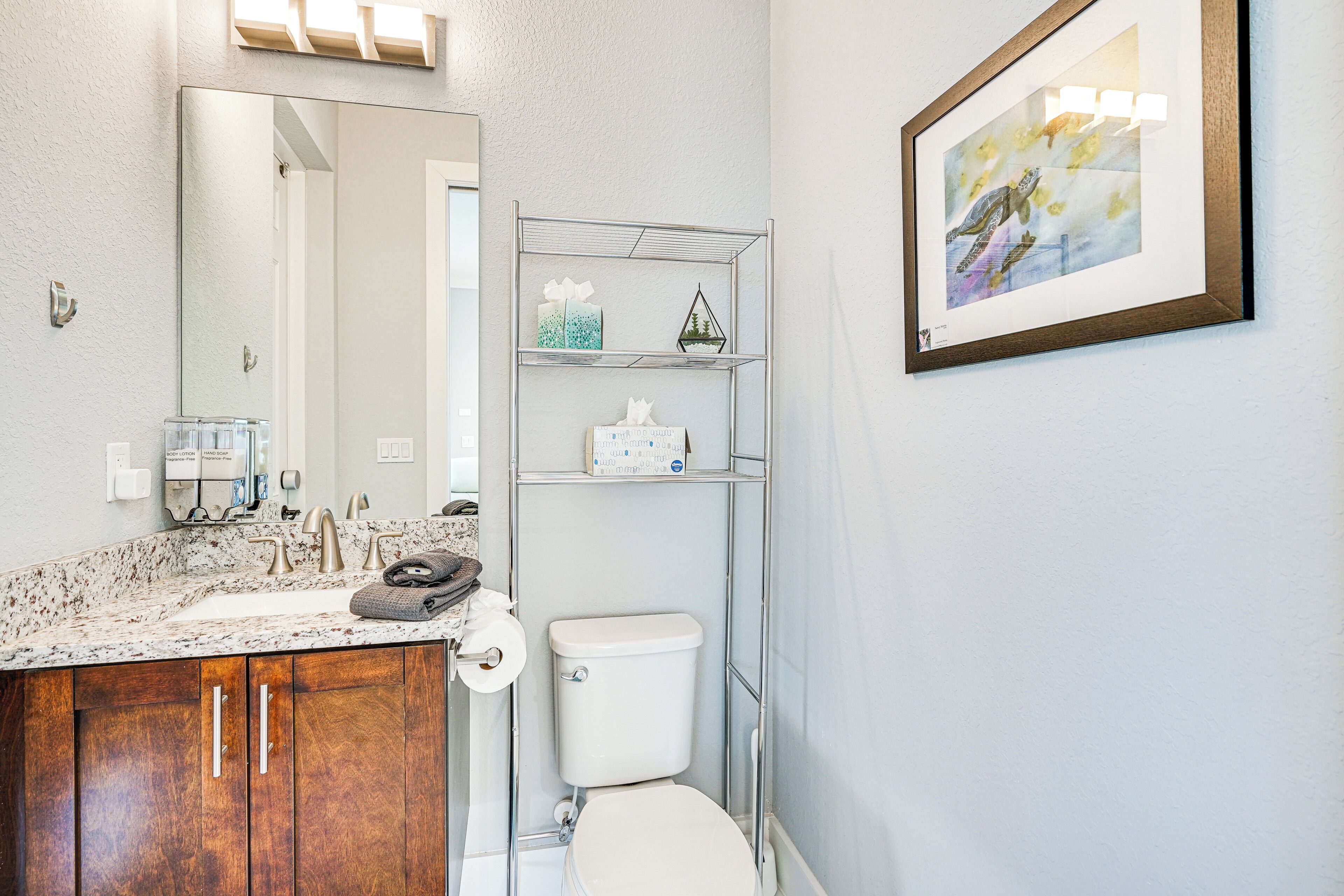 A bathroom with a marble sink, wooden cabinets, a toilet, and a shelf with toiletries.