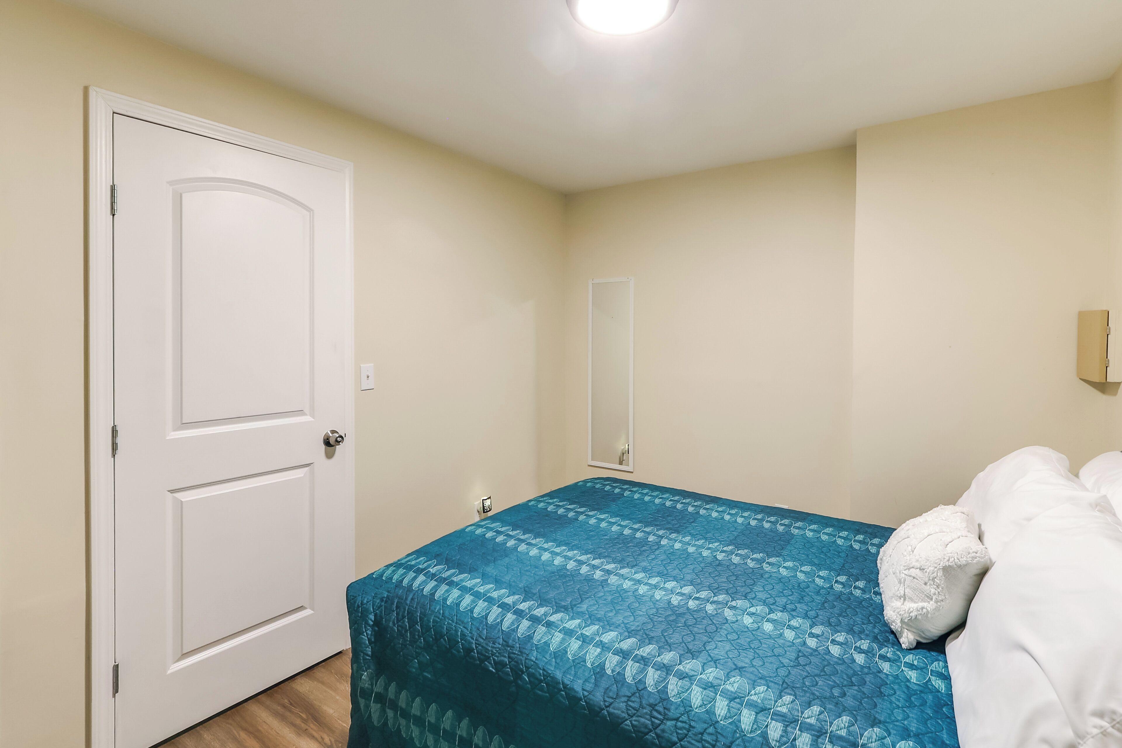 A bedroom with a bed, a door, and a mirror on the wall.