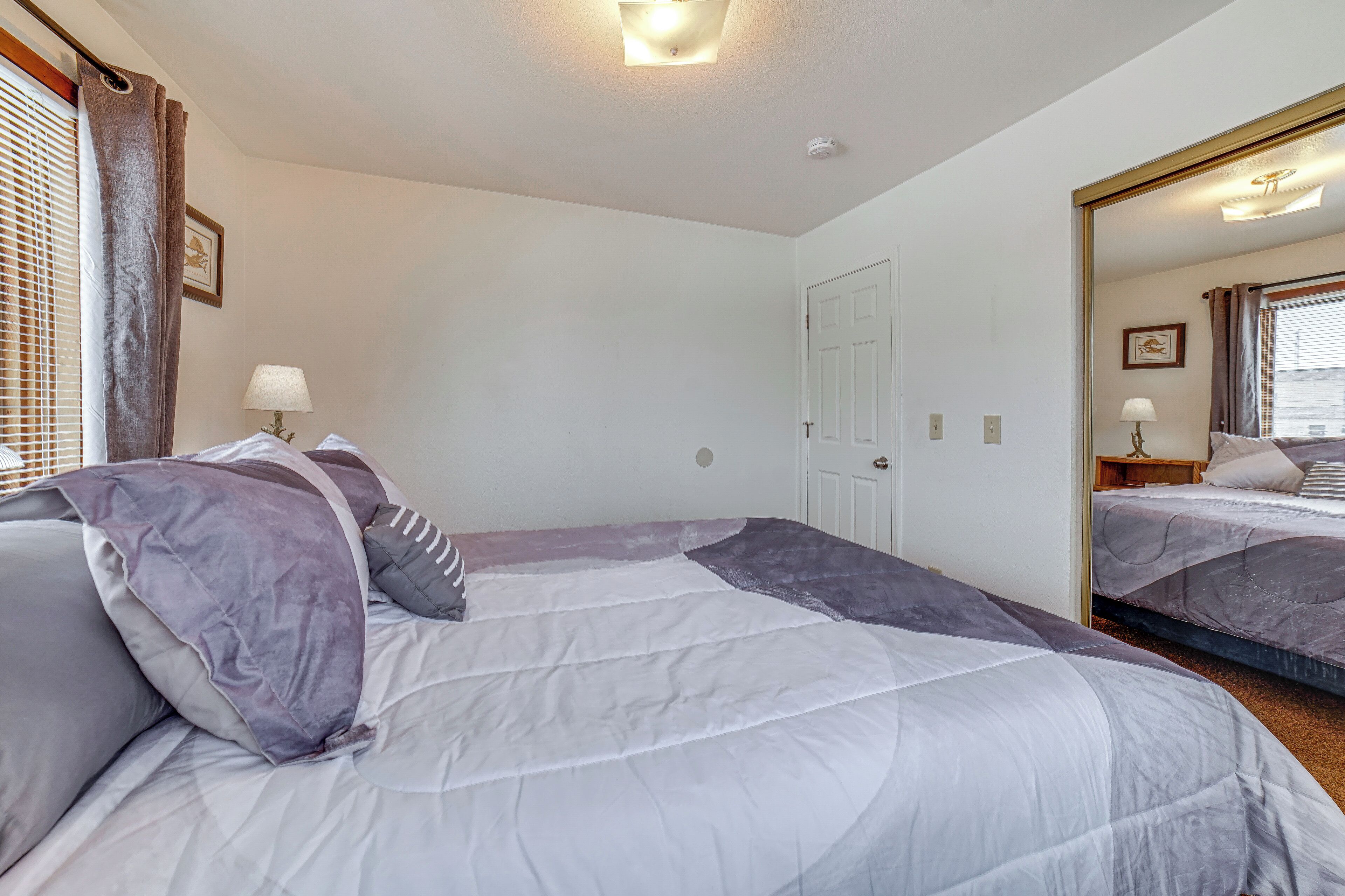 A hotel room with two beds, a large mirror, a door, and a window with blinds.
