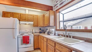 A kitchen with wooden cabinets, a white refrigerator, a stove, and a sink. - Cozy Anchorage Vacation Rental Near Hospitals! (Anchorage)