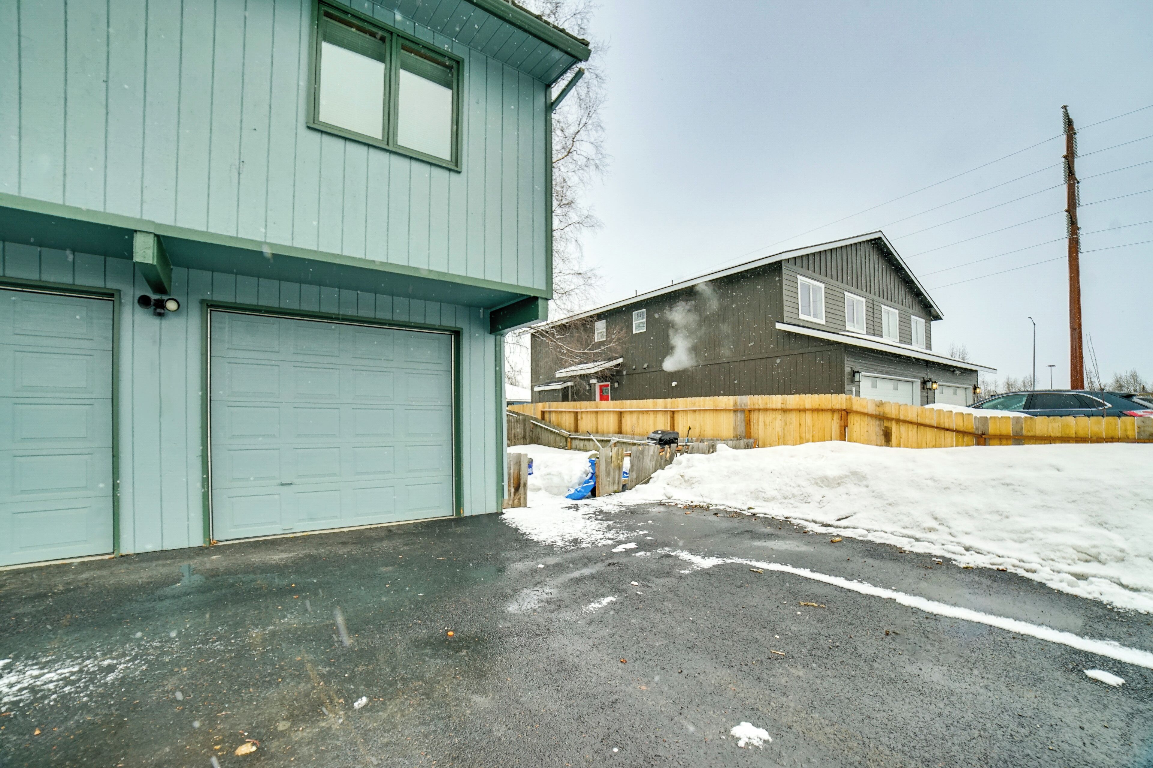 A residential area with a light blue garage, a grey house with a white garage door, and a wooden fence.