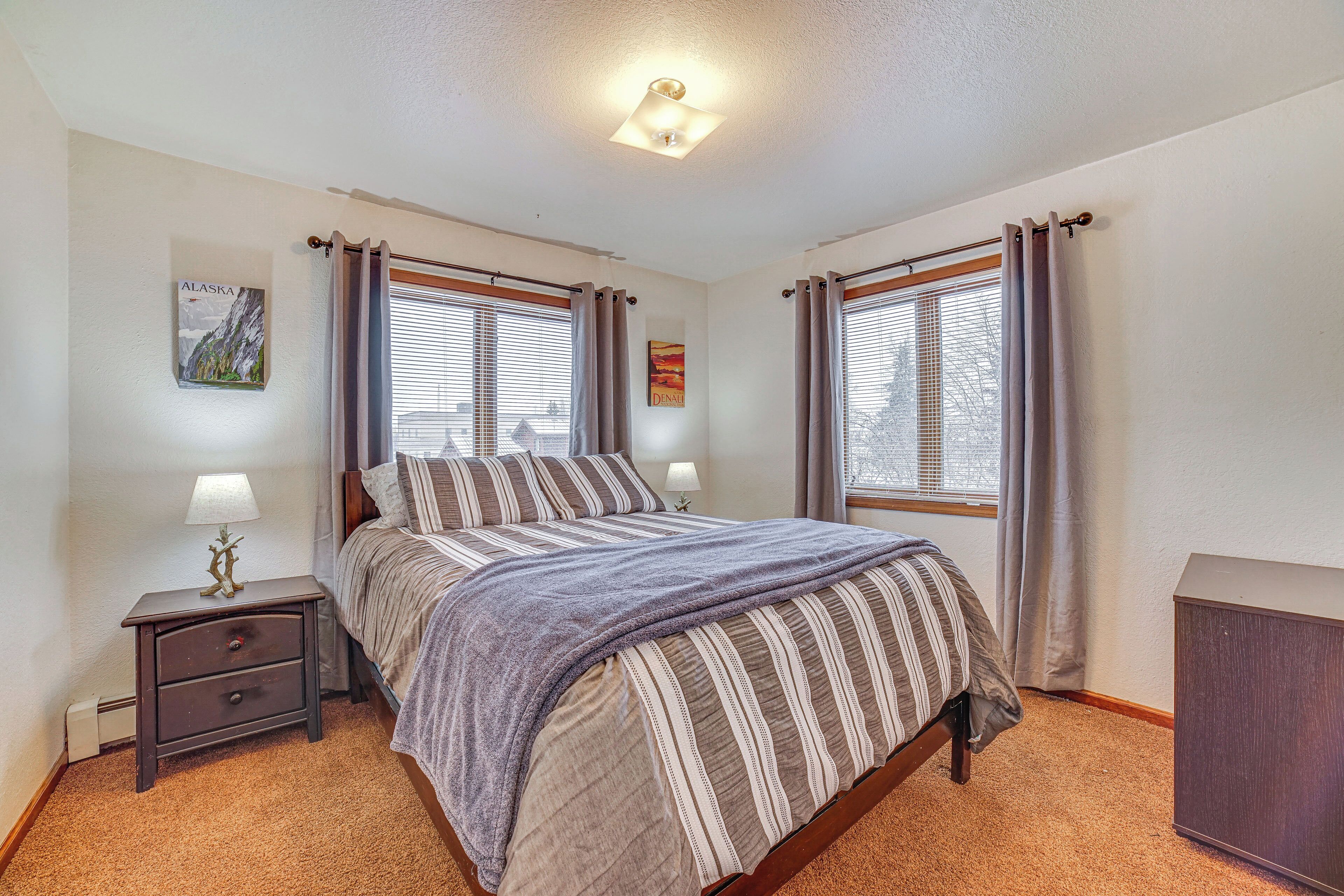 A bedroom with a bed, two bedside tables, a nightstand, a lamp, and a window with curtains.