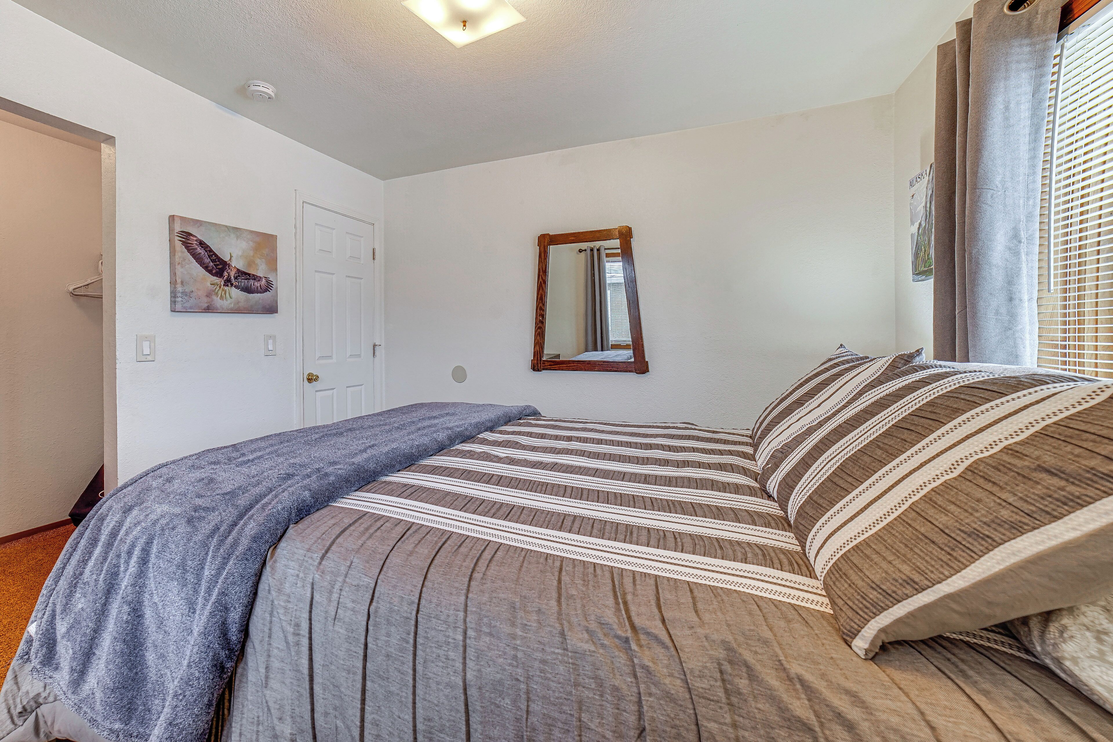 A bedroom with a bed, a window with curtains, a door, and a wall-mounted mirror.