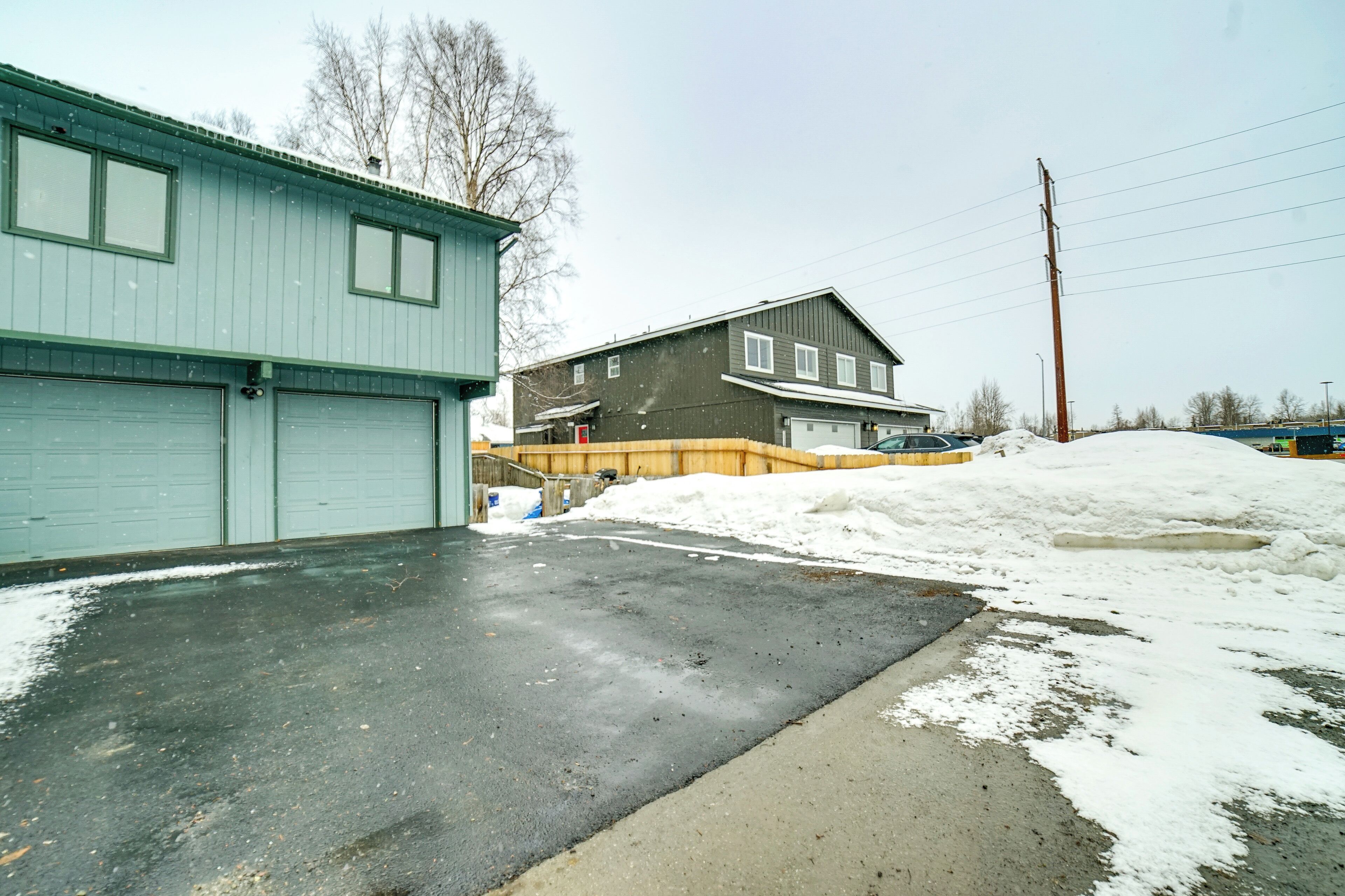 A garage with a snow-covered driveway and a house in the background.