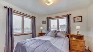 A bedroom with a bed, two bedside tables, a nightstand, a lamp, and a window with curtains. - Cozy Anchorage Vacation Rental Near Hospitals! (Anchorage)