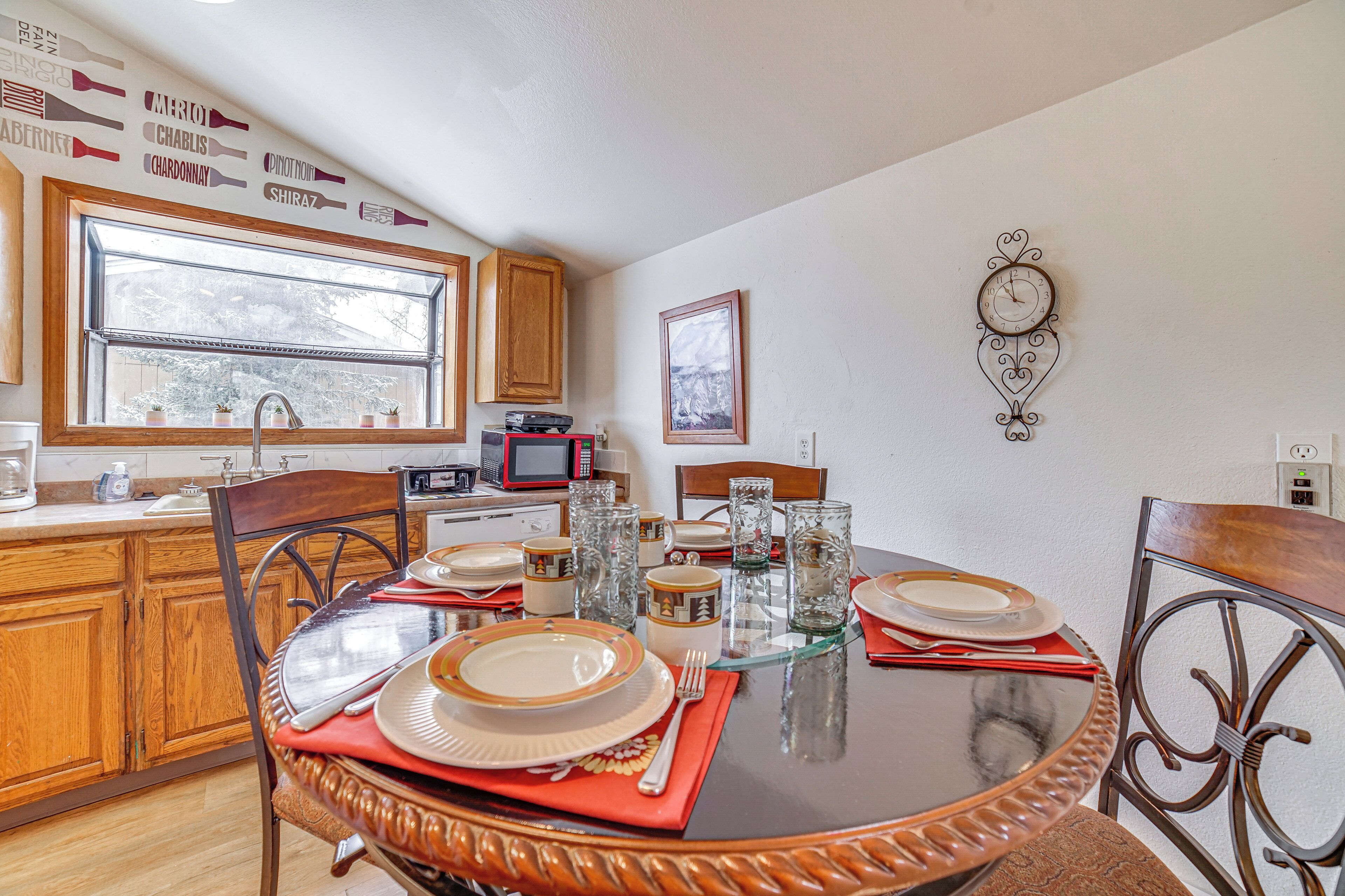 Un comedor con una mesa redonda dispuesta para cuatro, sillas de madera y una cocina al fondo.
