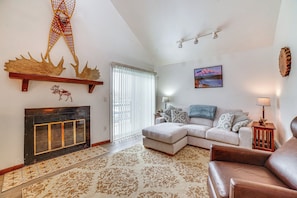 A living room with a fireplace, a sofa, a coffee table, and a decorative wall hanging. - Cozy Anchorage Vacation Rental Near Hospitals! (Anchorage)