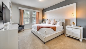 Une chambre à coucher avec un grand lit, une table de chevet, une commode et un téléviseur fixé au mur.
