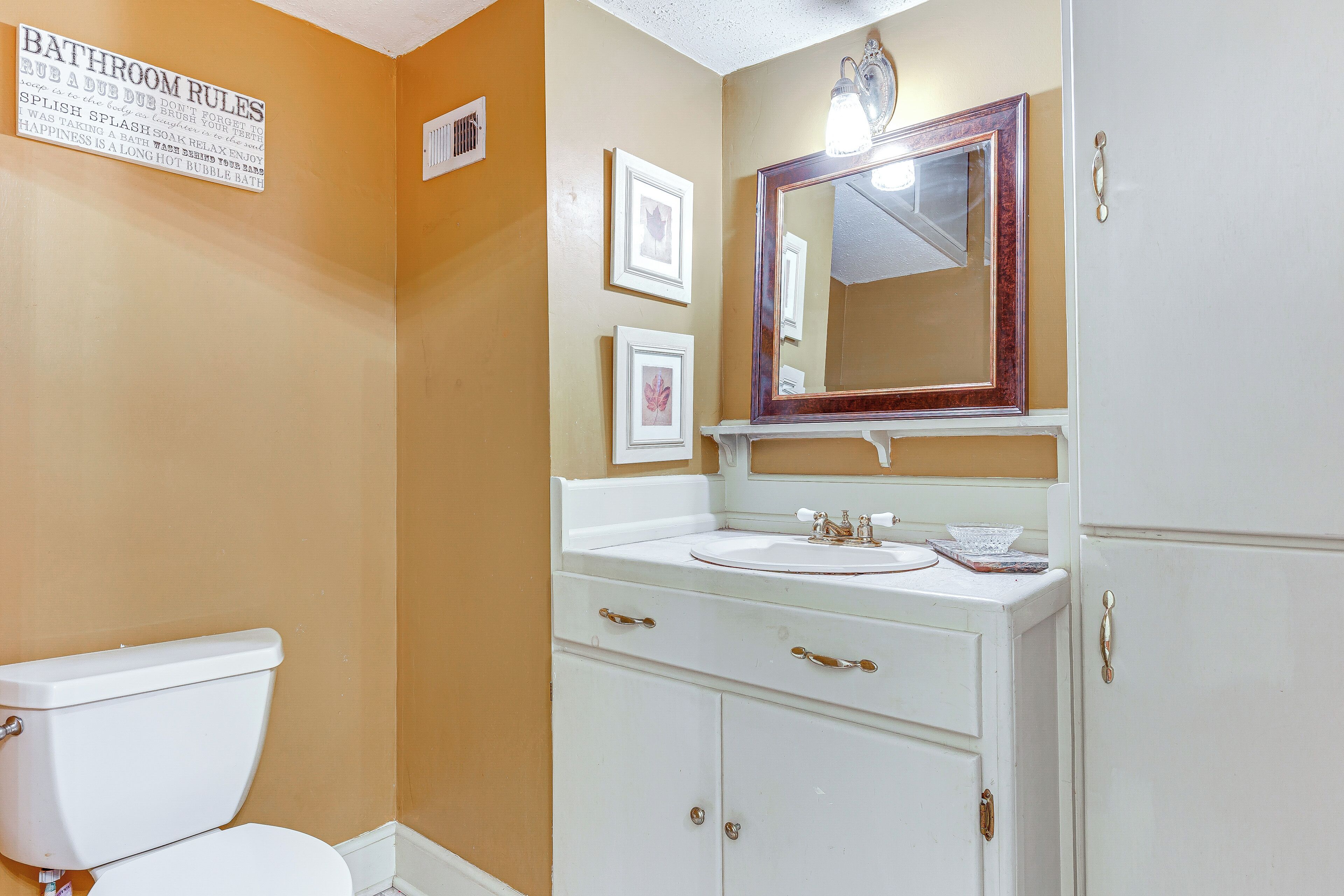 A bathroom with a toilet, sink, and cabinet. There is a sign on the wall and a mirror above the sink.