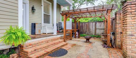 A patio with a wooden pergola, brick steps, and a potted plant.
