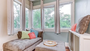 A cozy room with a sofa, ottoman, and a window with curtains.