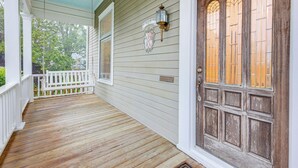 A porch with wooden flooring, a white railing, and a wooden door with glass panels.