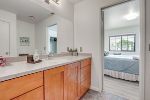 A bathroom with a large mirror, wooden cabinets, a countertop, and a window.