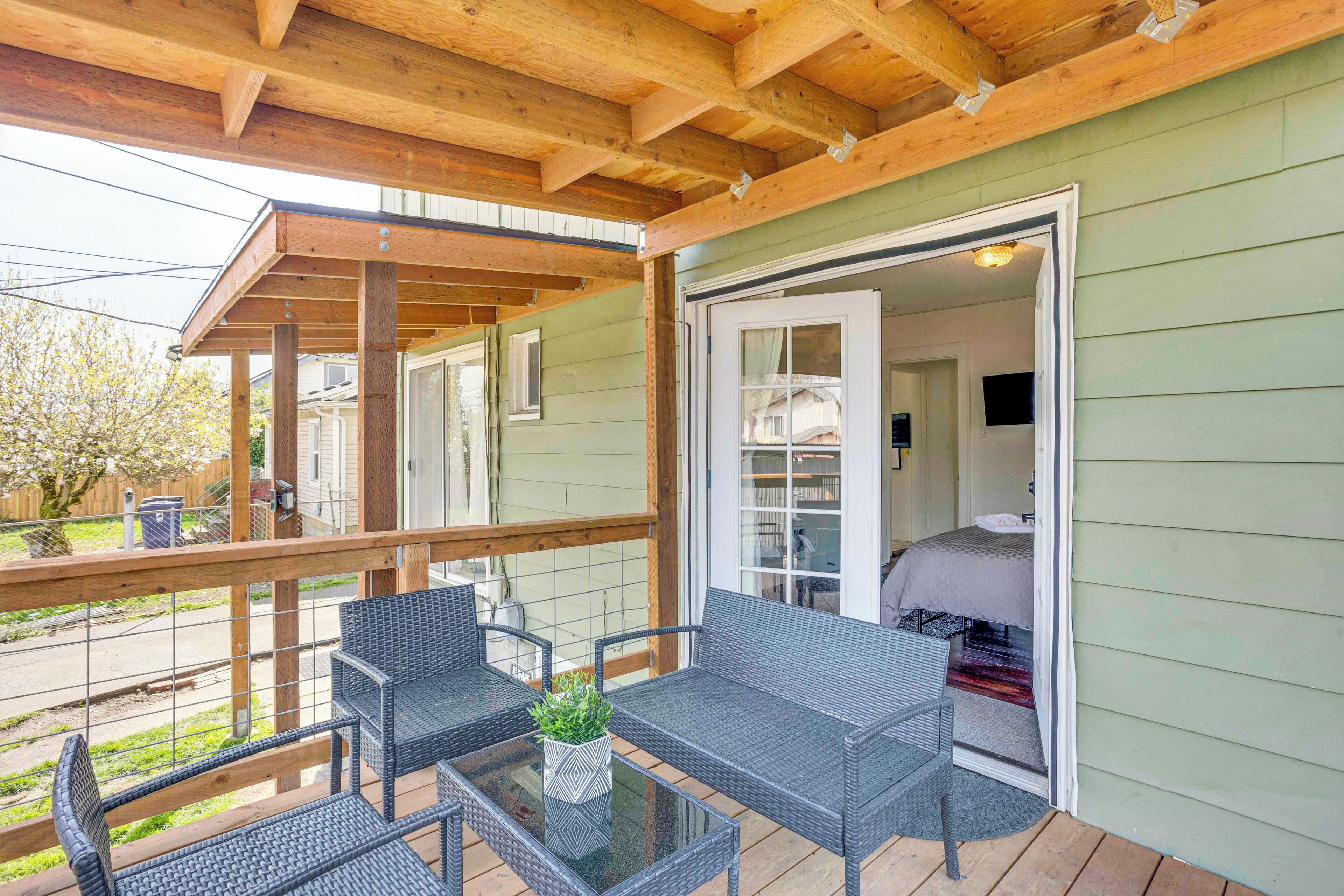 A covered porch with wicker furniture and a glass table, leading to a room with a bed and a TV.