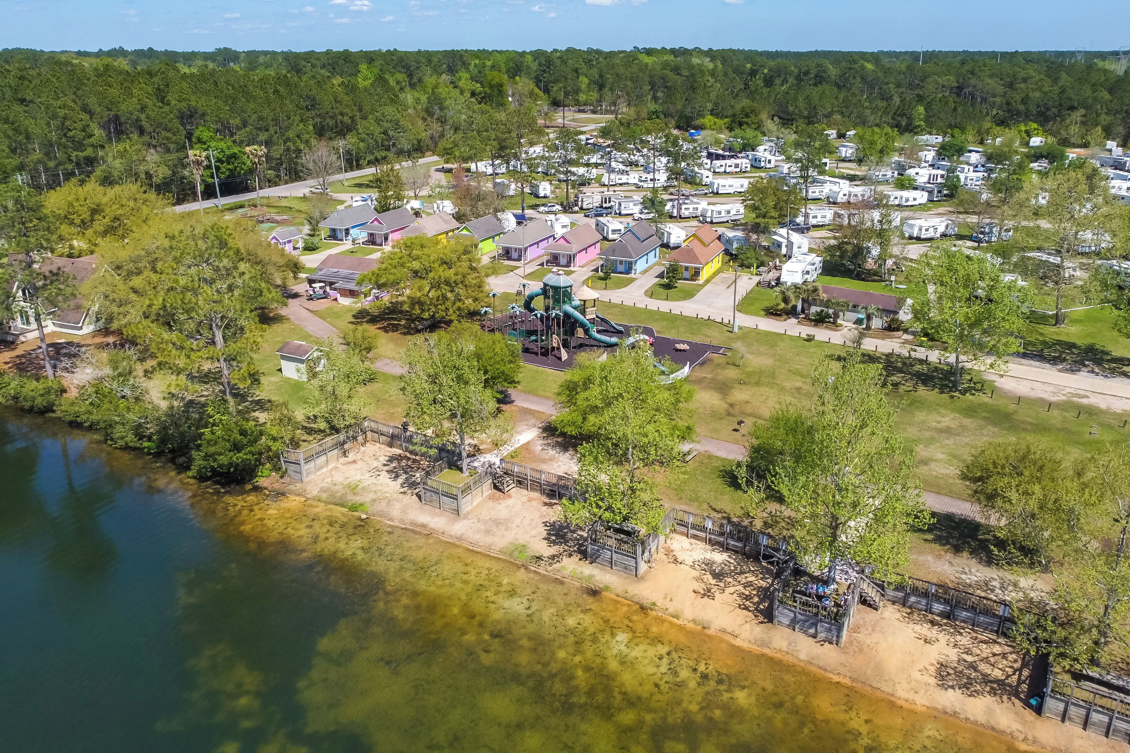 A lakeside campground with RVs and cabins, a playground, and a walking path along the water.