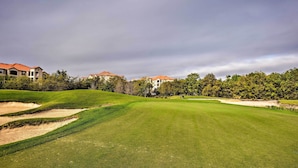 Ein Golfplatz mit gepflegtem Rasen, Sandbunkern und Wohnhäusern im Hintergrund.