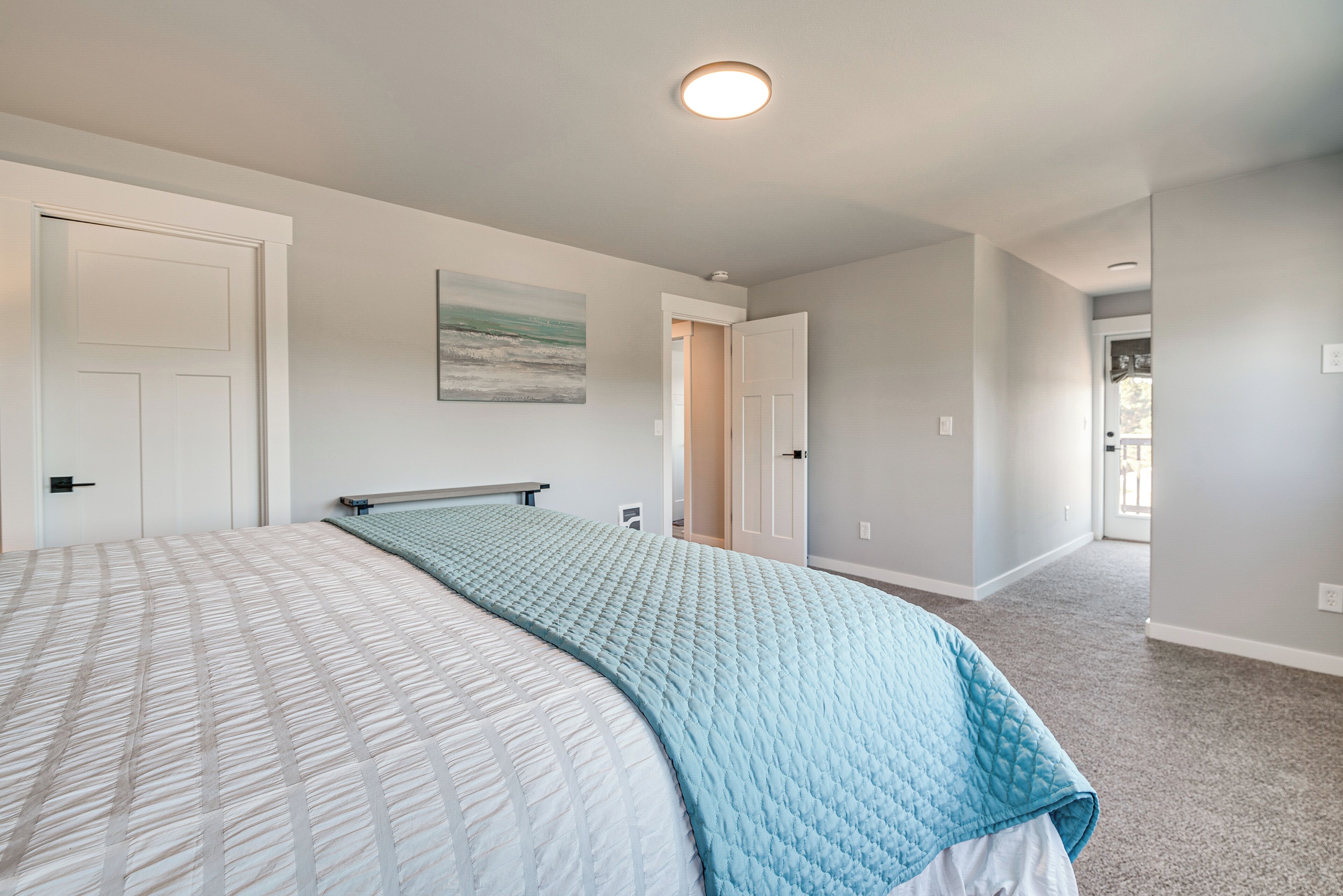 A bedroom with a bed, a door, and a hallway leading to another room.