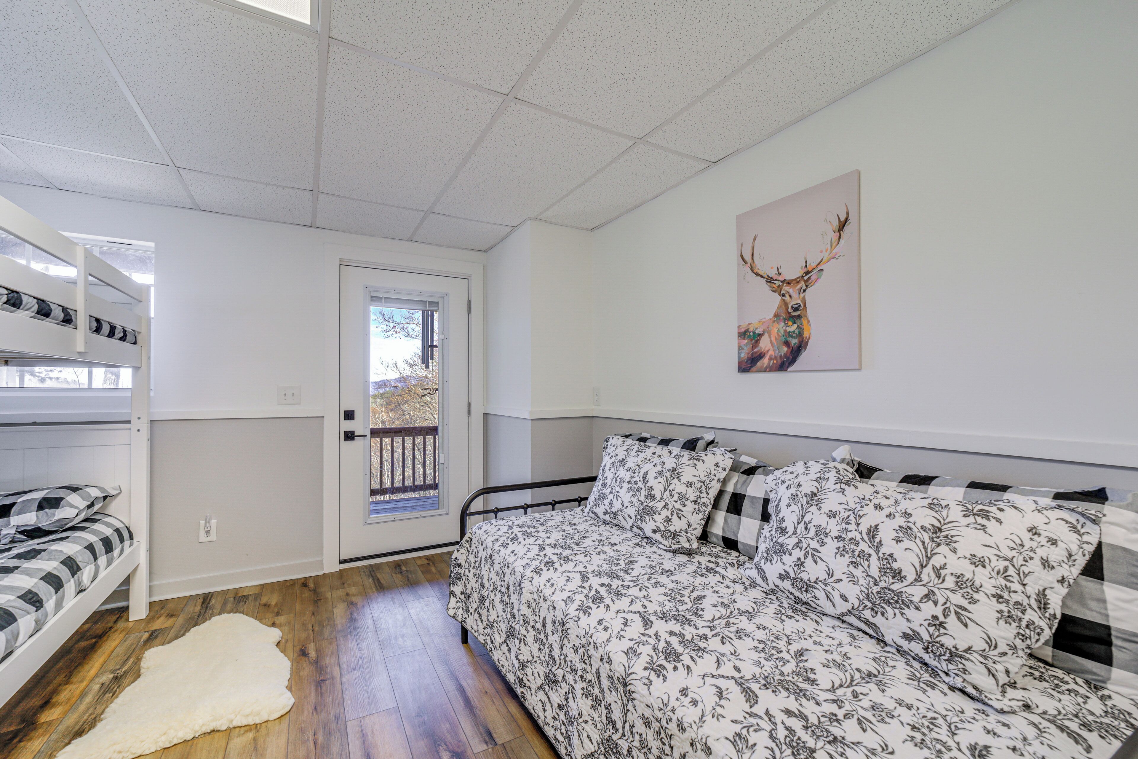 A bedroom with a bed, a window, a door, and a wall-mounted deer painting.