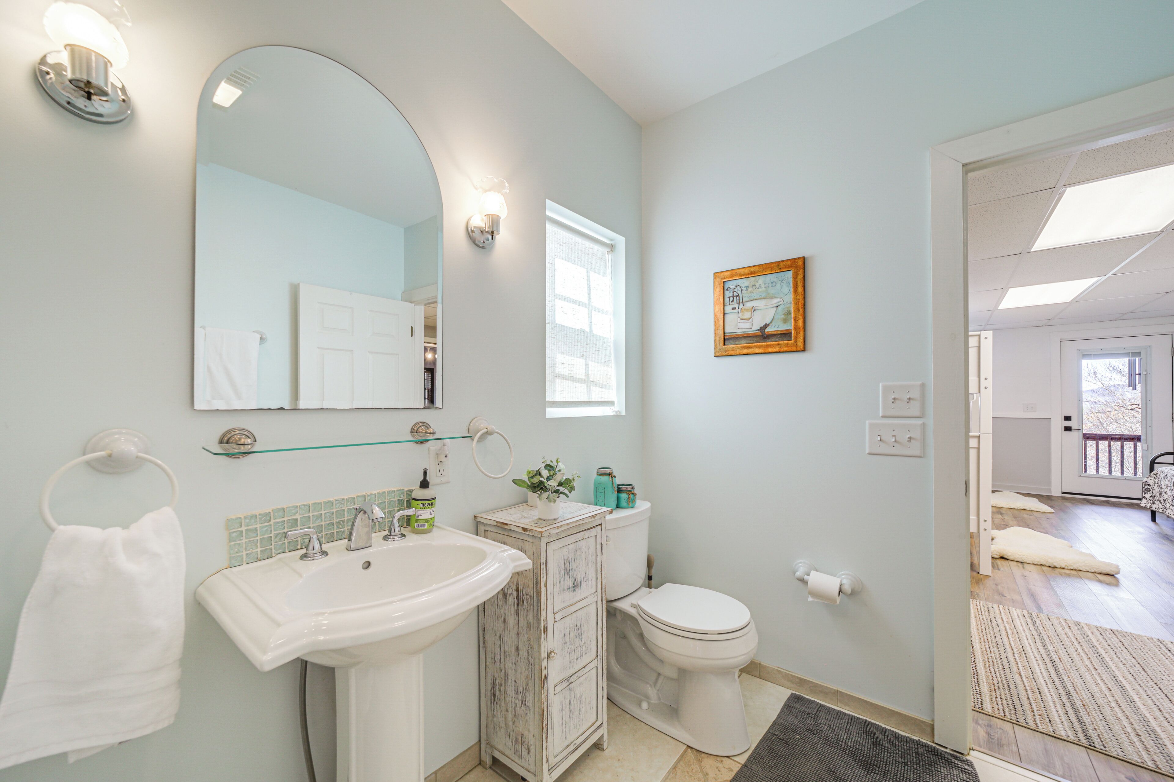 A bathroom with a sink, mirror, toilet, and a small window.
