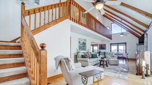A spacious living area with a wooden staircase, a ceiling fan, and a large window providing natural light. - Sky Valley Retreat w/ Fire Pit & Mountain Views! (Dillard)