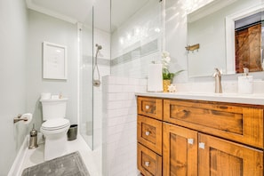Un baño moderno con cabina de ducha de vidrio, paredes con azulejos blancos y un tocador de madera con cajones.