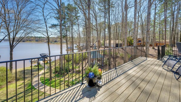 A wooden deck with a railing overlooking a lake, surrounded by trees and a small gazebo.