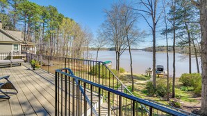 A deck with outdoor seating, a view of a lake, and a boat docked nearby.
