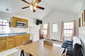 A modern kitchen with wooden cabinets, a microwave, and a ceiling fan. There is a dining area with a table and chairs, and a black sofa. - Charming Biloxi Studio w/ Community Pool & Lake! (Biloxi)