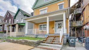 A two-story house with a green roof, a porch with white railings, and a brick facade. - Cozy East Pittsburgh Home - 7 Mi to Frick Park! (East Pittsburgh)
