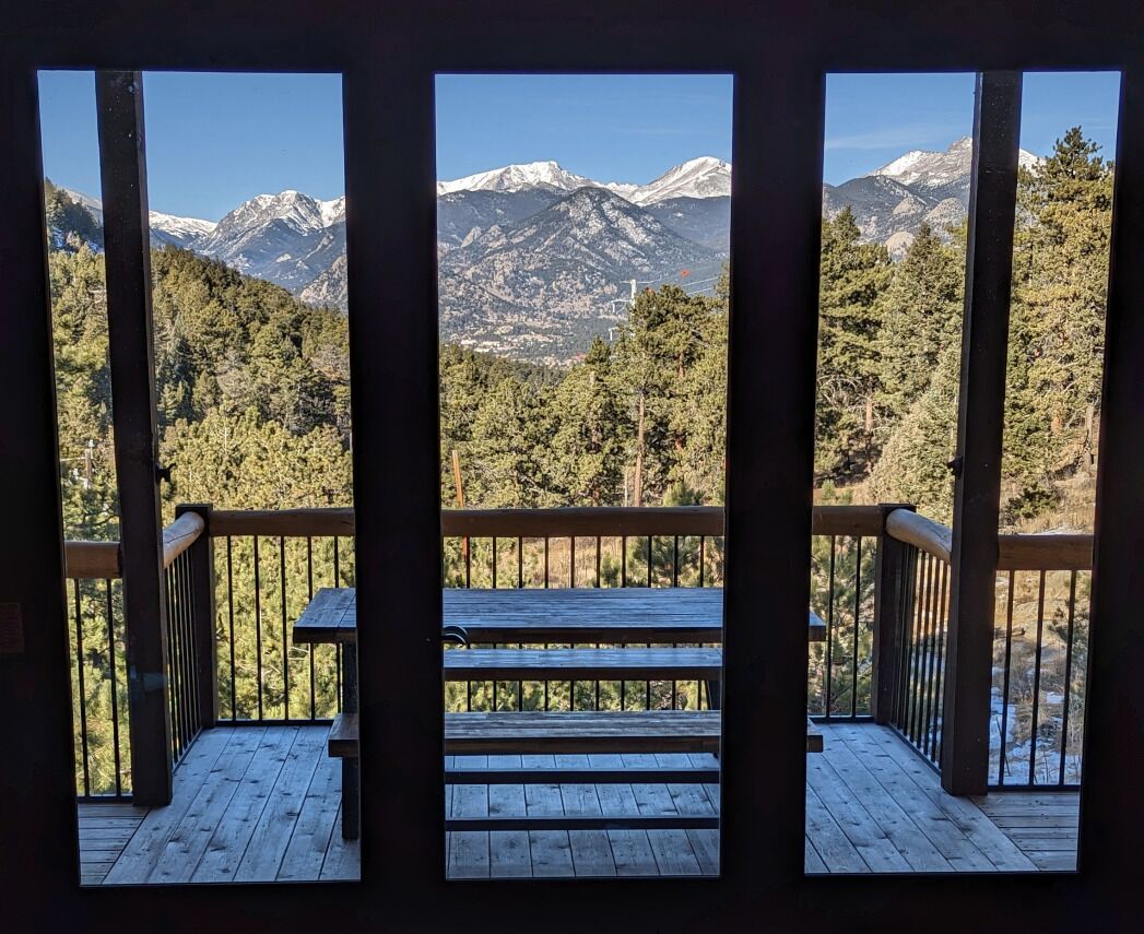 Une terrasse en bois avec un banc, offrant une vue sur un paysage montagneux aux sommets enneigés.