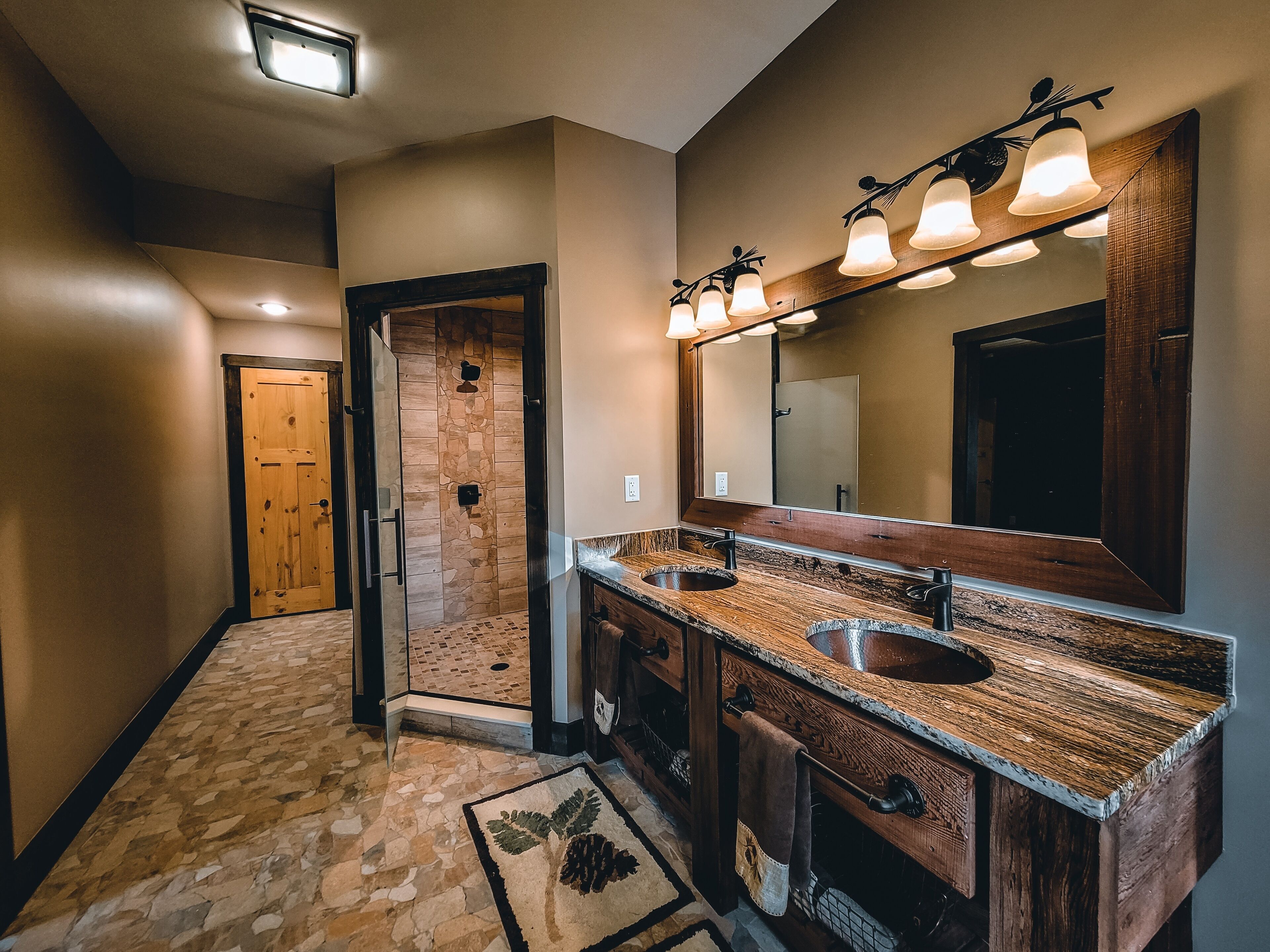 Un baño moderno con ducha de piedra, un espejo grande y un tocador de madera con dos lavamanos.