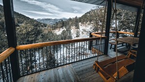 Eine Holzterrasse mit Blick auf schneebedeckte Berge und einen Wald.
