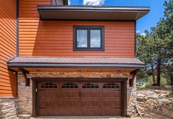 Una casa moderna con fachada de madera, base de piedra y un gran portón para coches.