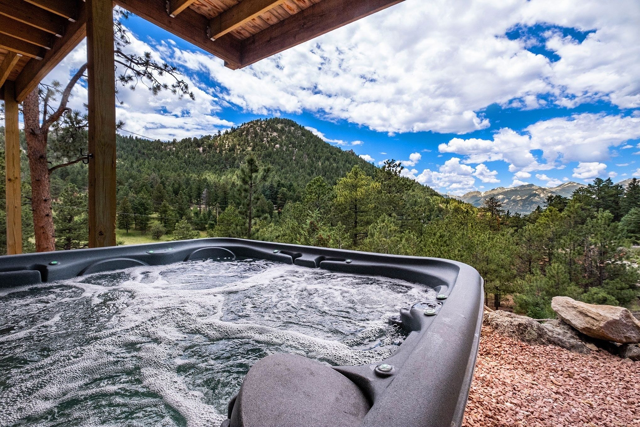 A hot tub with a mountain view, wooden pergola, and natural surroundings.