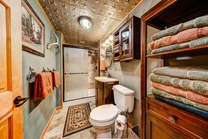 A bathroom with a toilet, sink, and shower. There are towels stacked on a shelf and a rug on the floor. - Longs Peak Cabin - Monthly Long-term Vacation Rental 30+ Days -- Estes Park 3 Bedroom Cabin by RedAwning (Estes Park)