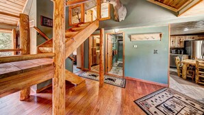 Un intérieur en bois avec un escalier, une tête de cerf fixée au mur et un coin repas.