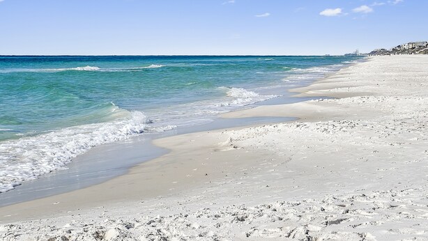 A beach with clear water, a sandy shore, and a distant building. - 30a Hideaway 2 Bedroom Townhouse by RedAwning (Panama City Beach)