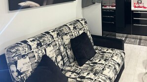 A modern living room with a black and white patterned sofa, a large framed artwork on the wall, and a black cabinet with drawers. - Vacation House at Mely's (Marsala)