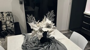 A dining area with a white table, a black cabinet, and a vase with white flowers. - Vacation House at Mely's (Marsala)